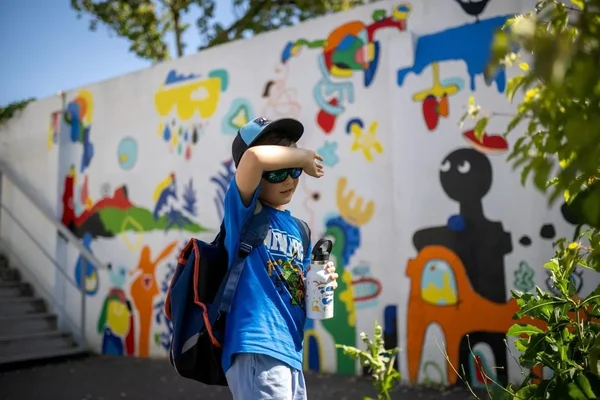 Un enfant se protège de la chaleur avec une bouteille d'eau et des lunettes de soleil, illustrant les gestes de précaution face à la canicule.