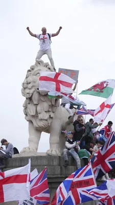 Homme en t-shirt de la croix de saint Georges, bras levés, perché sur un lion en pierre lors du rassemblement.