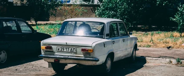Une VAZ-2101 blanche avec une plaque bulgare garée sur un terrain vague, illustrant le marché automobile russe en crise.