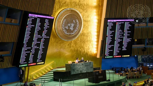 Salle de l'Assemblée générale de l'ONU pendant un vote, avec écrans et podium.