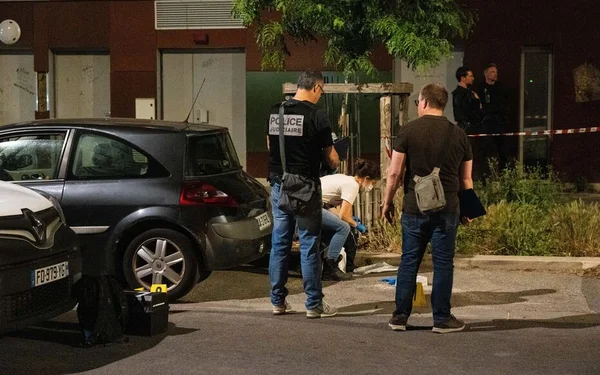 Enquête de police judiciaire de nuit sur un parking, près d'un véhicule suspect.