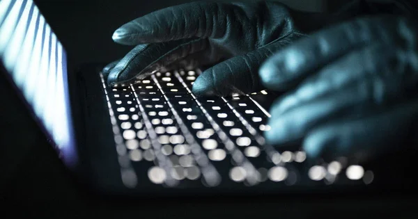 Mains gantées tapant sur un clavier d'ordinateur dans l'obscurité, illustrant une activité de piratage.