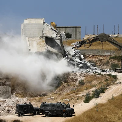 Israël détruit des maisons palestiniennes en territoire occupé : une excavatrice en action avec des véhicules militaires.