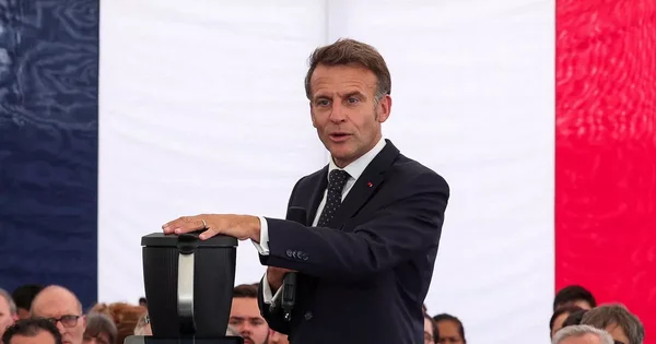 Emmanuel Macron s'exprimant lors d'un événement officiel en extérieur avec le drapeau français.
