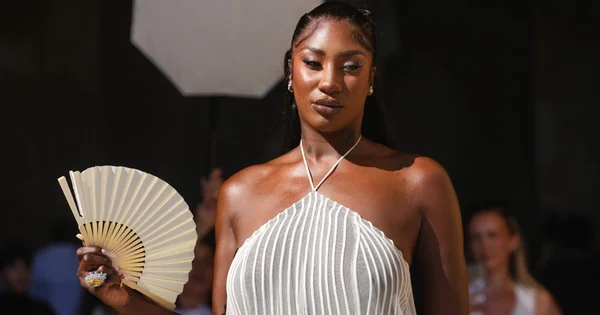 Aya Nakamura en robe blanche plissée, éventail à la main, lors d'un événement.
