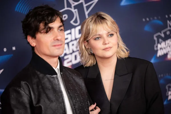 Louane et Florian Rossi en tenue décontractée devant un fond bleu.