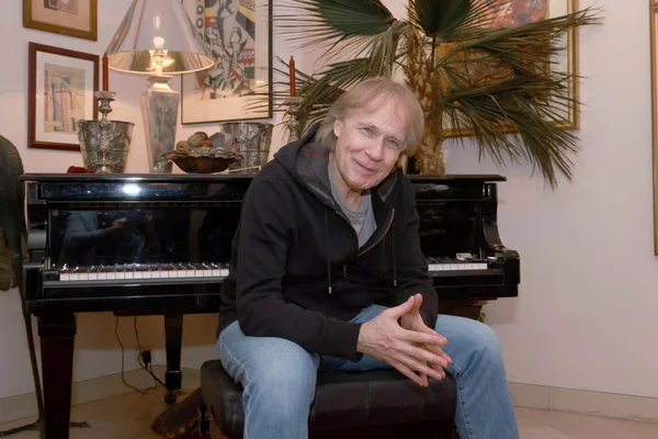 Richard Clayderman dans un cadre intimiste, vêtu d'un sweat à capuche, assis devant son piano.
