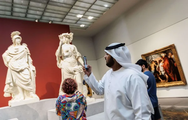 Visiteur photographiant des statues antiques au Louvre Abu Dhabi.