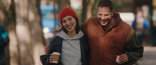 Scène du film 'Tout va super' : Hakim Jemili et Noémie Lvovsky déambulant avec des cafés.