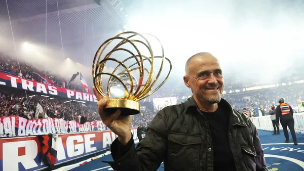 Luis Enrique célébrant un trophée avec les supporters du PSG dans un stade animé.