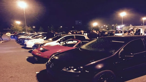 Rassemblement de voitures modifiées de nuit, avec une Volkswagen Golf noire en vedette.