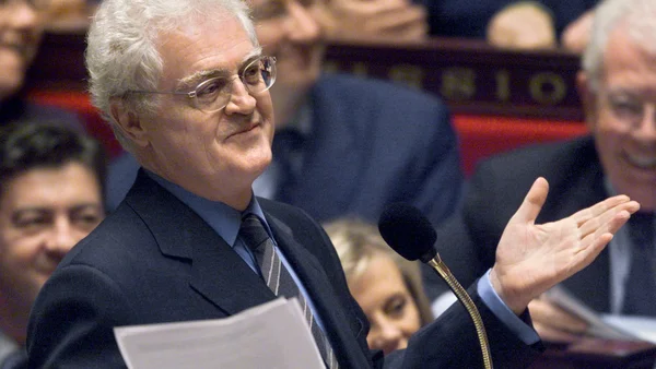 Lionel Jospin prenant la parole dans une assemblée, micro et documents en main.
