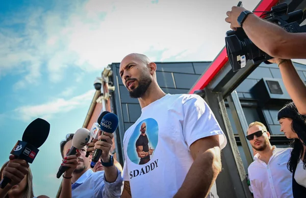 Andrew Tate répond aux questions des médias, t-shirt '$DADDY' visible.