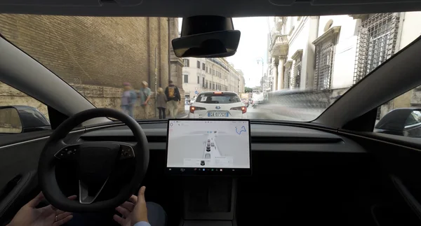 Conduite d'une Tesla en ville, vue depuis le poste de conduite avec l'écran de navigation.