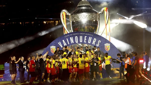 Les joueurs du RC Lens célèbrent leur victoire en Coupe de France devant le trophée et le panneau 'VAINQUEURS'.