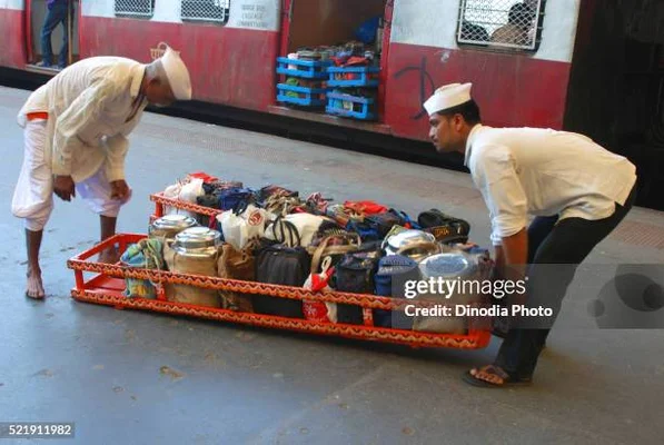 Dabbawalas transportant des bagages sur un quai de gare à Mumbai, témoignant de leur rôle logistique étendu.