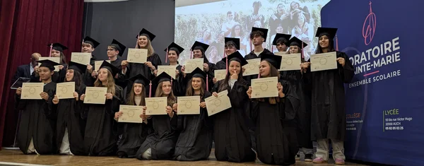 Étudiants diplômés en toges noires posant avec leurs certificats lors de la cérémonie à l'Oratoire Sainte-Marie d'Auch.