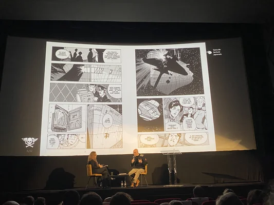 Alex Alice et une intervenante lors d'une présentation de son manga sur scène.