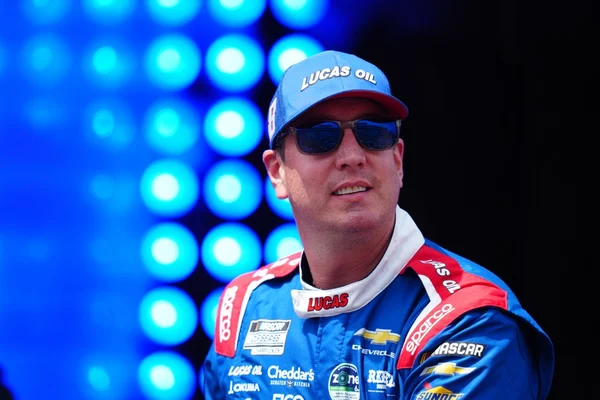 Kyle Busch en tenue LUCAS OIL devant un éclairage scénique.