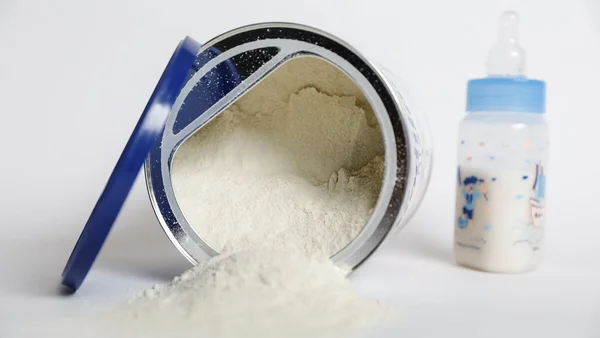 Boîte de lait infantile renversée avec poudre répandue et un biberon à côté.