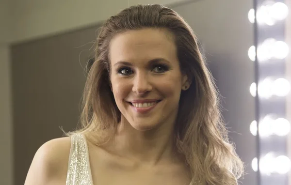 Lorie souriant devant un miroir de maquillage, vêtue d'un haut scintillant.