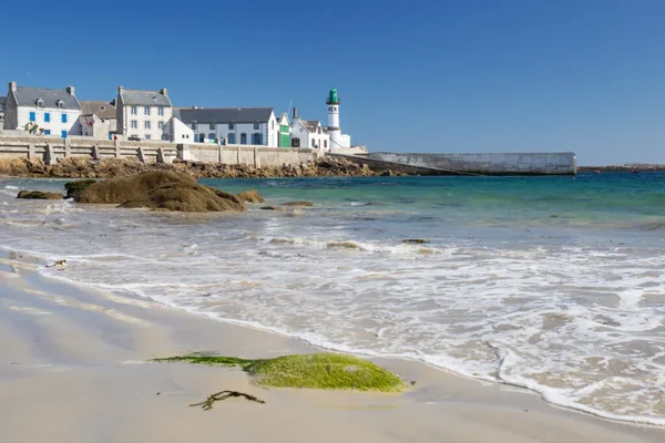 Plage et port de l'île de Sein par beau temps, avec ses maisons blanches et son phare emblématique.