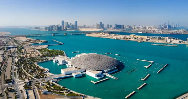 Vue aérienne du Louvre Abu Dhabi, son dôme géométrique et ses eaux turquoise.
