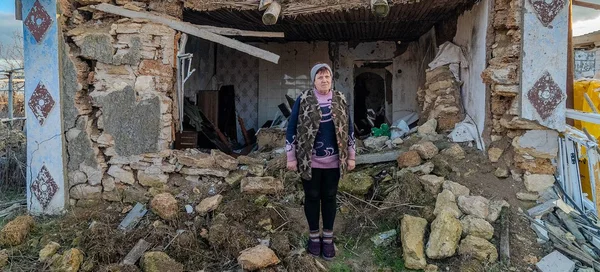 Femme âgée devant un bâtiment détruit par le conflit en Ukraine.