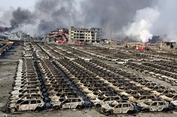 Conséquences d'une explosion massive dans un parc de stockage automobile en Chine, avec des centaines de véhicules détruits.