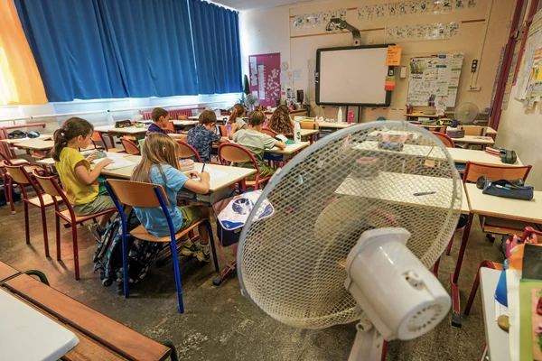 Des élèves travaillent en classe avec un ventilateur pour faire face à la canicule.
