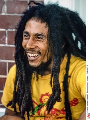Bob Marley souriant, t-shirt jaune, fond de briques.
