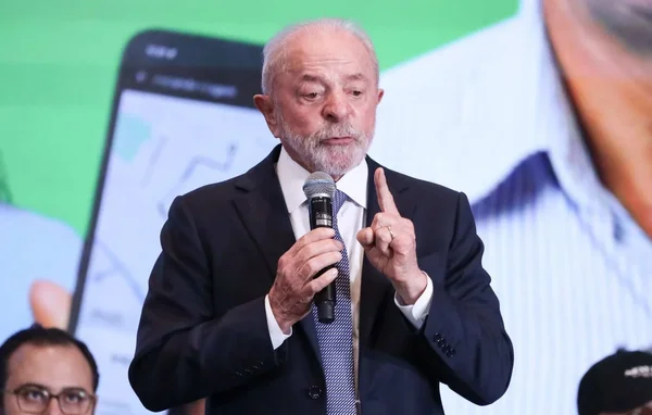 Lula s'exprimant lors d'une conférence, devant un écran montrant une interface de smartphone.