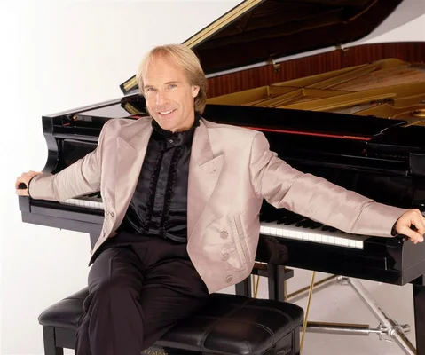 Richard Clayderman en tenue de scène, assis près d'un piano à queue.