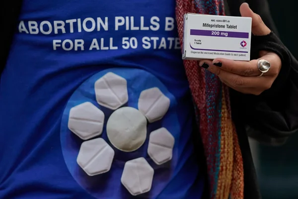 Un militant brandit une boîte de mifépristone devant un t-shirt revendiquant l'envoi postal de pilules abortives.