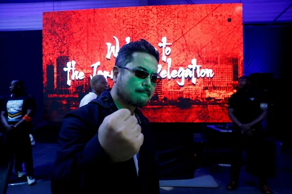 Katsuhiro Harada devant un écran LED lors d'un événement.