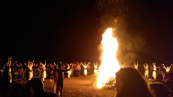 Feu de joie au Festival du feu de Beltane 2019, Calton Hill, Édimbourg. La Reine de Mai et l'Homme Vert réunis font face au feu, tandis que les danseurs s'arrêtent pour lever leurs bras vers le ciel.