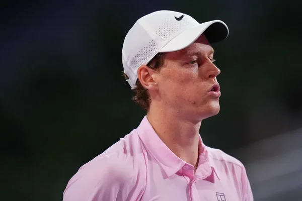 Jannik Sinner lors d'une conférence de presse, vêtu d'une casquette blanche Nike et d'une chemise rose.