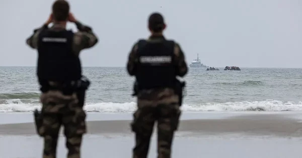 Des agents en uniforme sur une plage observent les opérations de secours après la mort de deux migrantes lors d'une tentative de traversée de la Manche.