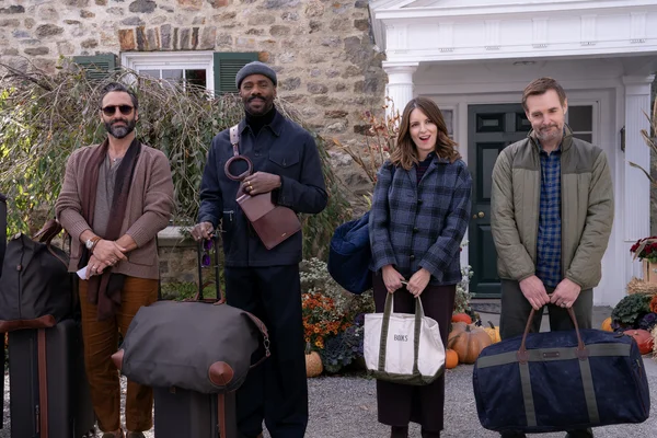 Scène de la série 'Les Quatre Saisons' montrant un groupe avec des bagages devant une maison décorée pour l'automne.