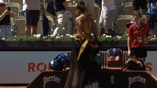 Naomi Osaka, vue de dos, arborant un haut scintillant doré et une jupe longue noire lors de son entrée sur le court.