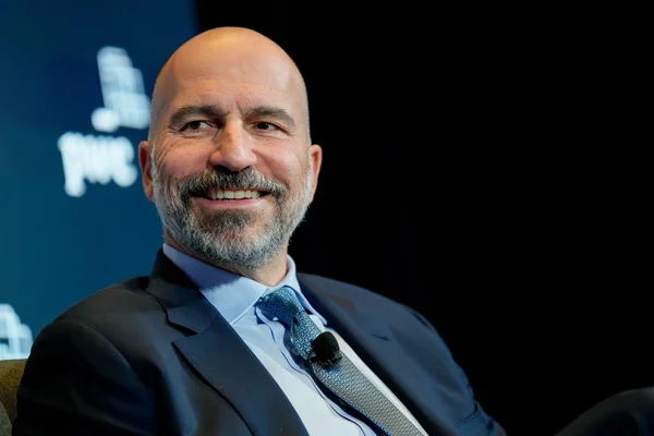 Dara Khosrowshahi souriant lors d'un événement avec le logo PwC en arrière-plan.