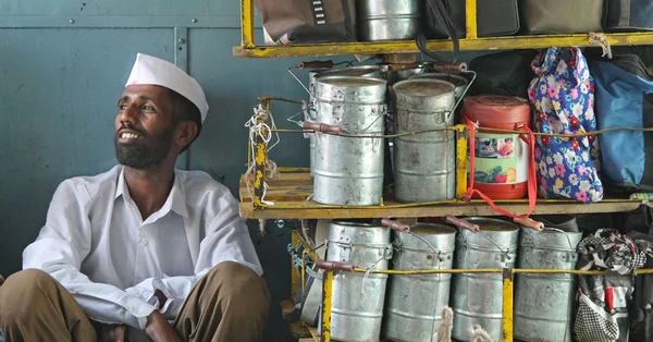 Dabbawala de Bombay se reposant près de tiffins empilés sur des étagères jaunes.