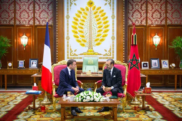Emmanuel Macron et le roi Mohammed VI lors d'une réunion officielle, entourés des drapeaux français et marocain.