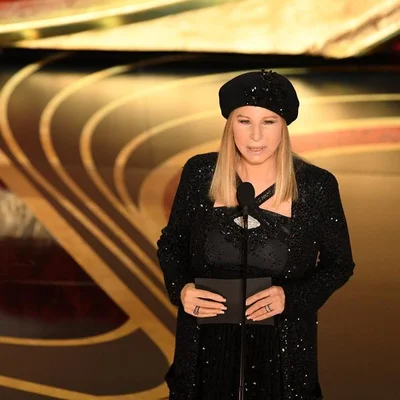 Barbra Streisand en tenue sequin et béret noirs, micro et carte noire, fond or et noir.
