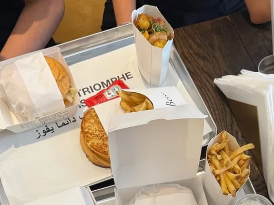 Un plateau de fast-food chic de Beau : burgers, frites et sauces servis sur un présentoir argenté.