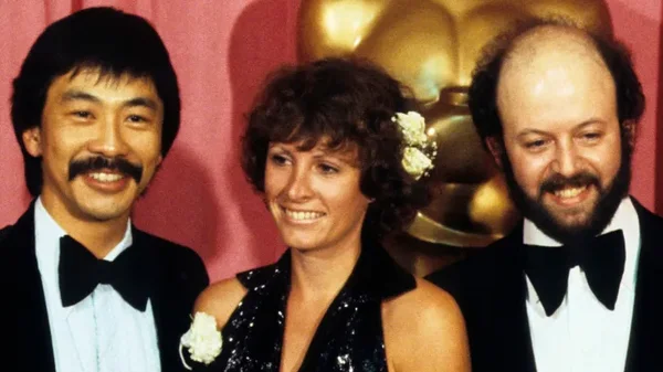 Marcia Lucas (centre) avec deux hommes lors d'une cérémonie, une statuette Oscar en arrière-plan.