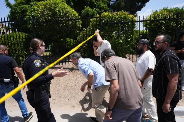 Un policier devant un ruban de sécurité jaune près de la mosquée de San Diego, avec des hommes rassemblés derrière la clôture