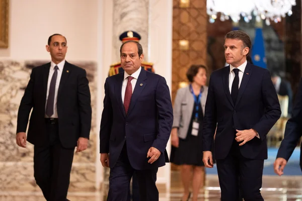 Emmanuel Macron et deux membres de sa délégation dans un couloir officiel à Alexandrie.