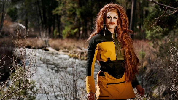 Pattie Gonia dans un cadre forestier, vêtue d'une veste jaune et noire