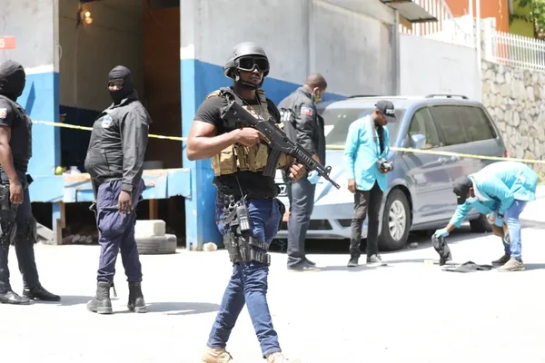 Un policier en tenue tactique et des enquêteurs médico-légaux examinent une scène de crime près d'une camionnette argentée après l'assassinat du président haïtien.